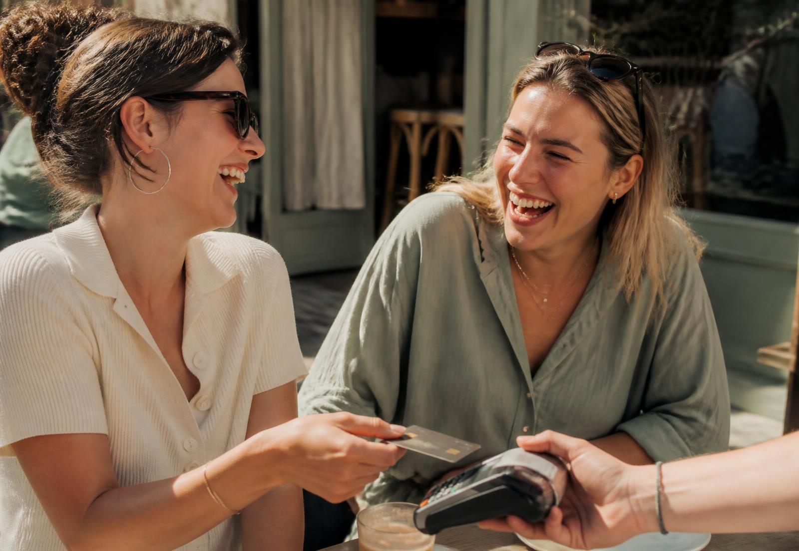 Two friends laughing while paying at an outdoor café
